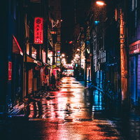深夜の路地裏に反射するネオンサイン看板と雨濡れた路面の写真
