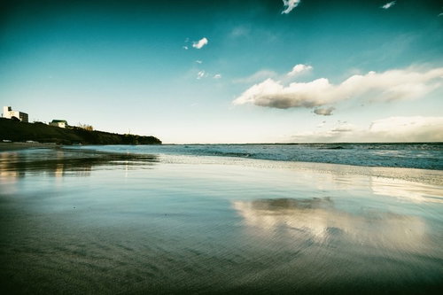 波が引くように去っていく砂浜と青い空