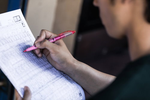 競馬新聞で予想を書き込む手元とピンク色のペン