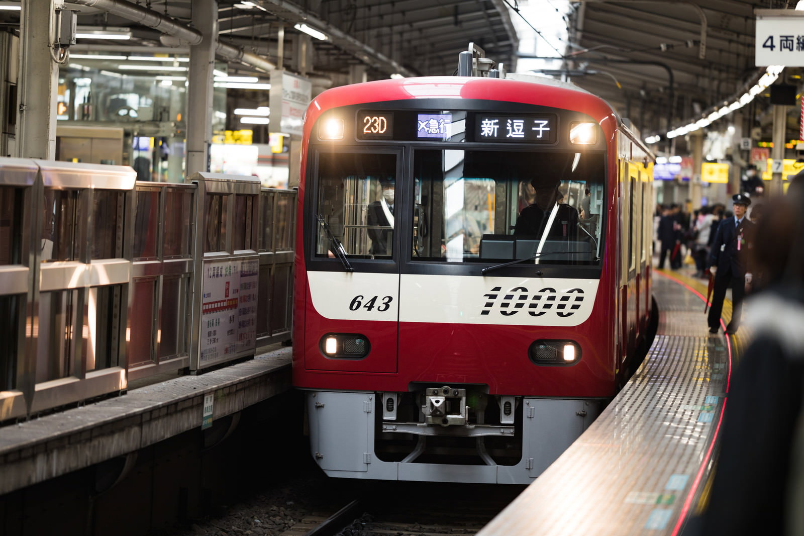 駅のホームに到着した赤い京急電車と通勤客の様子