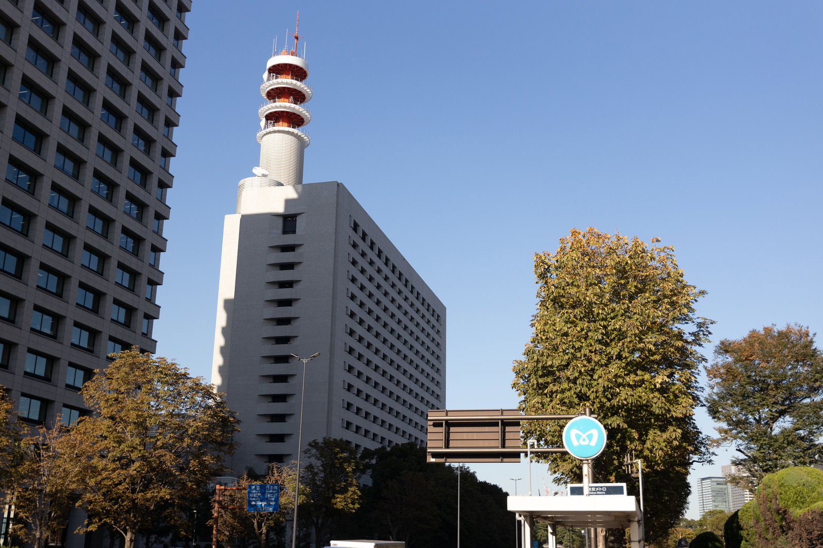 青空の下に建つ警視庁本部庁舎と煙突、周辺の秋の樹木