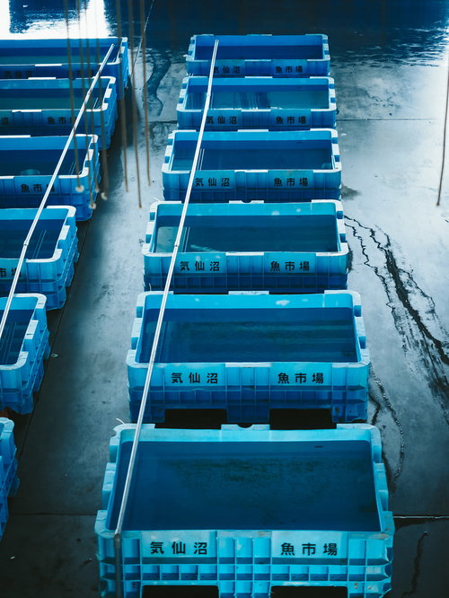 漁港に整然と並ぶ空の青いプラスチック水槽