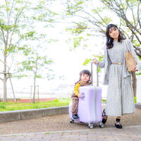 明るい春の陽気、キャリーケースを引く女性のおでかけスタイルの写真