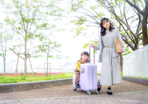 明るい春の陽気、キャリーケースを引く女性のおでかけスタイル