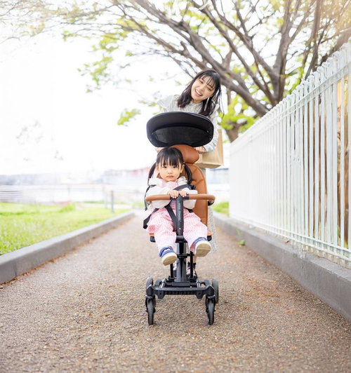 公園で黒いコンパクトベビーカーを持ち歩く紺ジャケットの女性