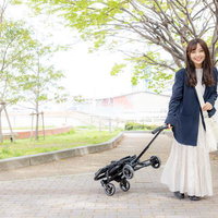 白いキッズトラベルキャリーを引く女の子と両親の新緑散歩の写真