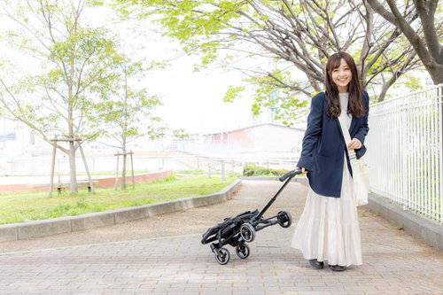 白いキッズトラベルキャリーを引く女の子と両親の新緑散歩