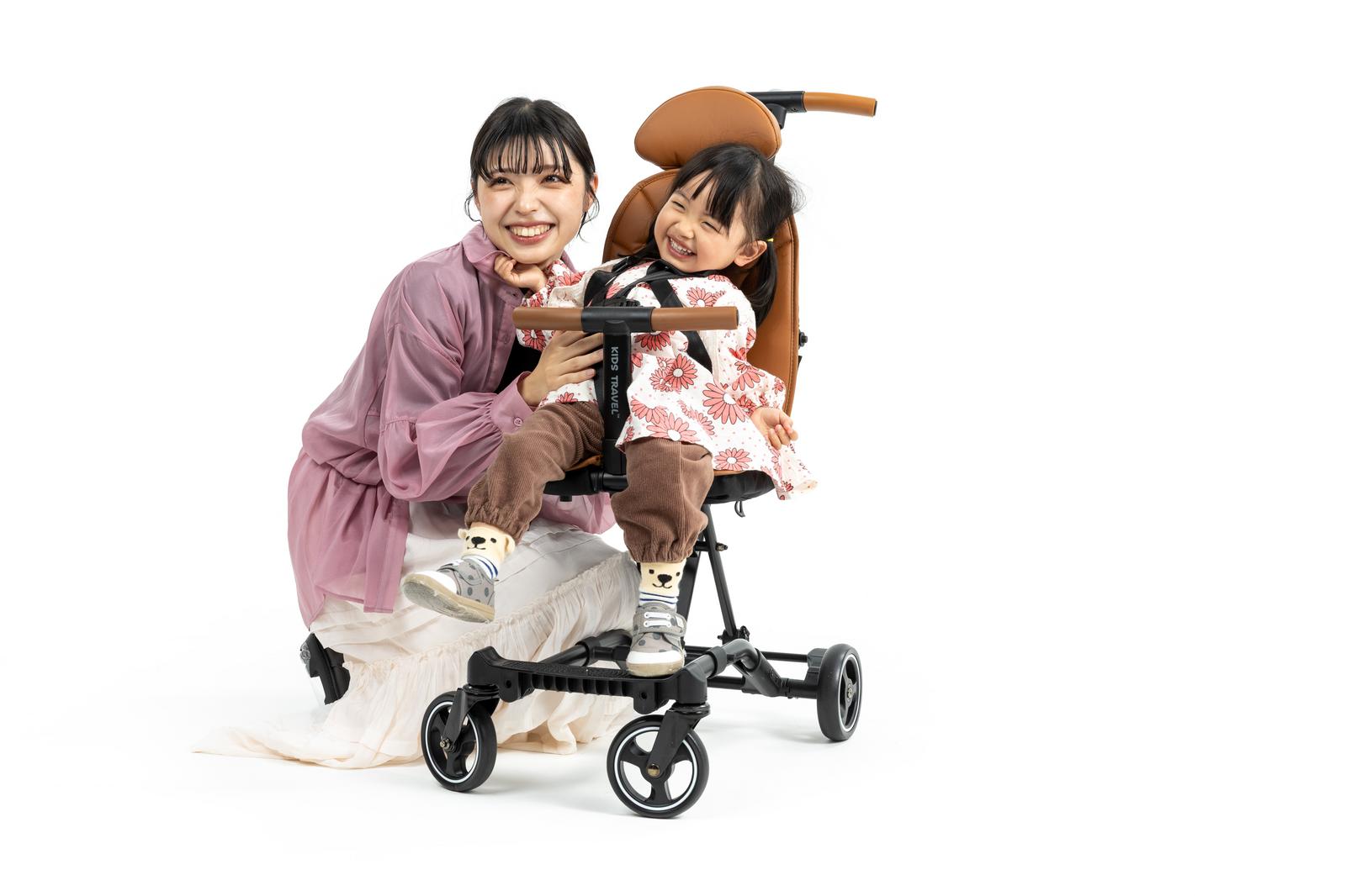 白背景でベビーカーのライドモードに乗って遊ぶ花柄服の女の子［モデル：高尾実生］