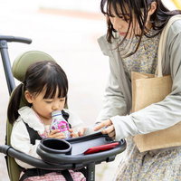 新緑の公園道でベビーカーを押す女性と子どもの写真