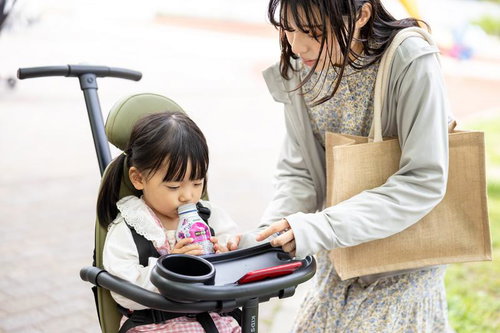 新緑の公園道でベビーカーを押す女性と子ども