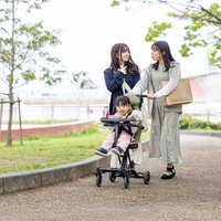 緑色のベビーカーに乗りピンクの服を着た女の子と母親の外出風景の写真