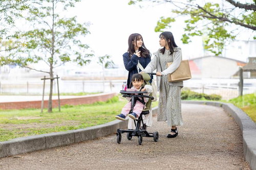 緑色のベビーカーに乗りピンクの服を着た女の子と母親の外出風景