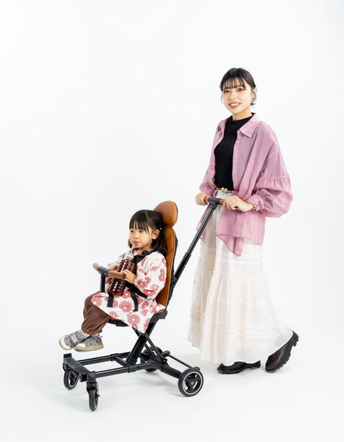 ピンクシャツの母親とB型ベビーカーに座る花柄ワンピースの女の子