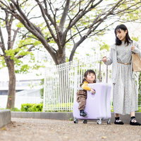 スーツケースに乗る幼児と母親の春のお出かけ風景の写真
