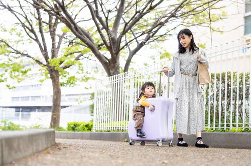 スーツケースに乗る幼児と母親の春のお出かけ風景