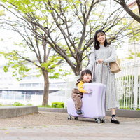 キャリーケースの上で微笑む子どもとお母さんの写真