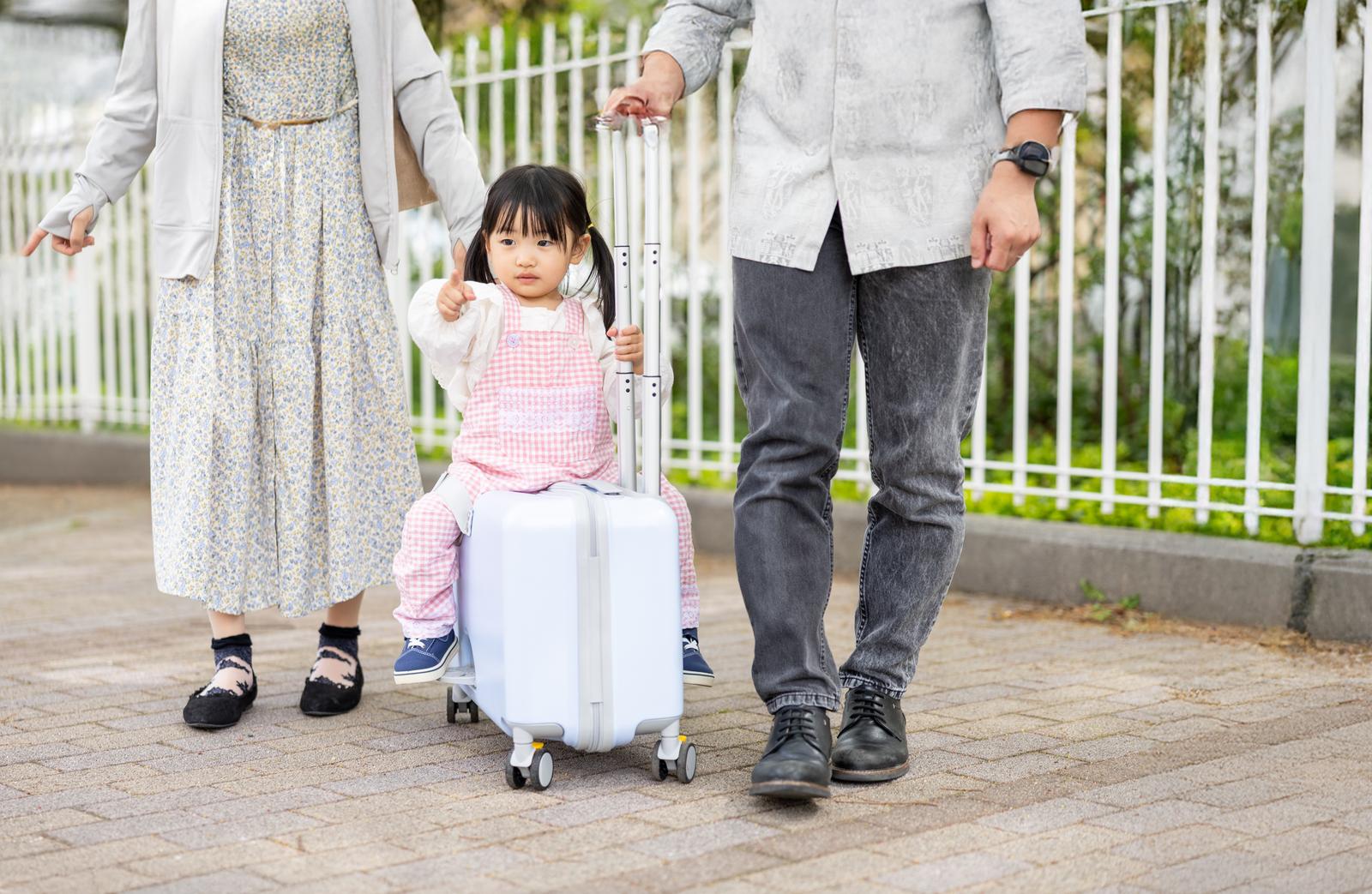 キャリーケースに座る女の子と両親が手を繋いで歩く家族