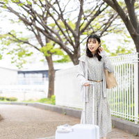 白いキャリーケースを引く花柄ワンピースの女性の写真