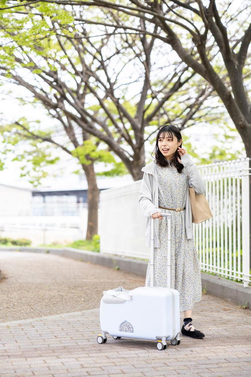 白いキャリーケースを引く花柄ワンピースの女性