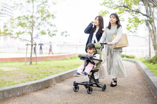 新緑の公園でベビーカーに乗る女の子と楽しく会話するママ友二人