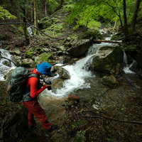 渓流で撮影する赤いウェアのカメラマンの写真