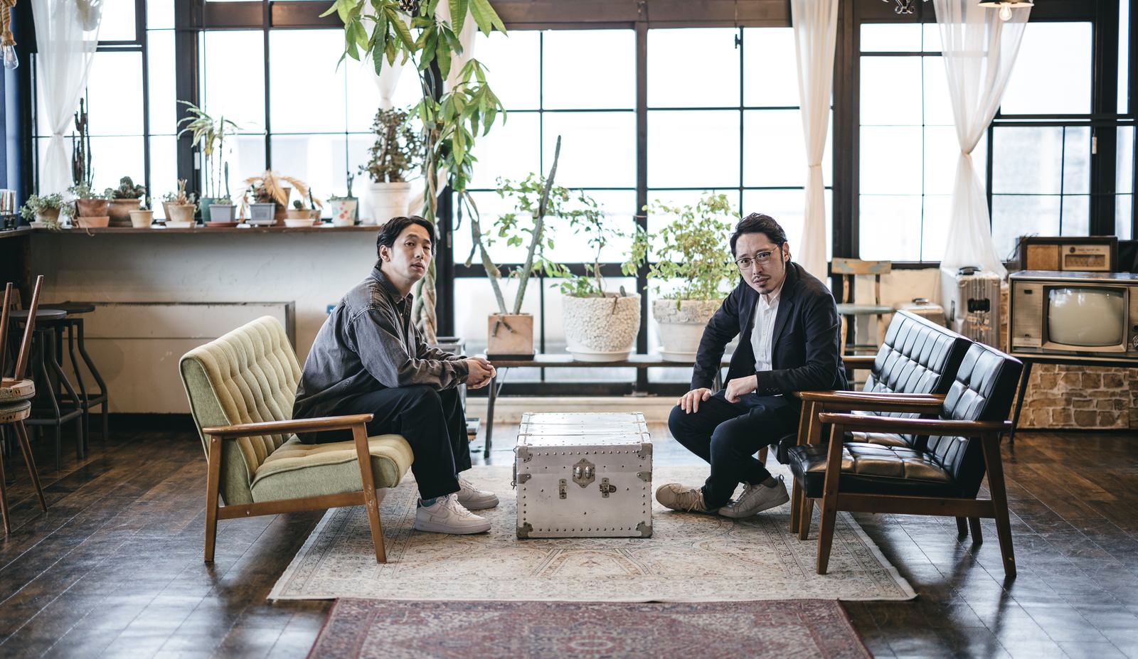 オフィスの明るい窓際で向かい合って座り相談している二人の男性［モデル：ゆうせい 大川竜弥］