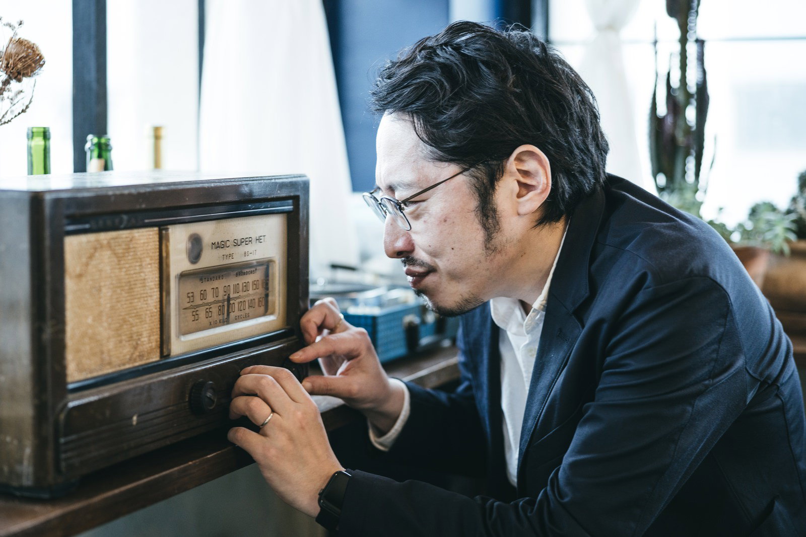 デスクでスーツを着た男性が古いラジオのダイヤルを調整している［モデル：ゆうせい］