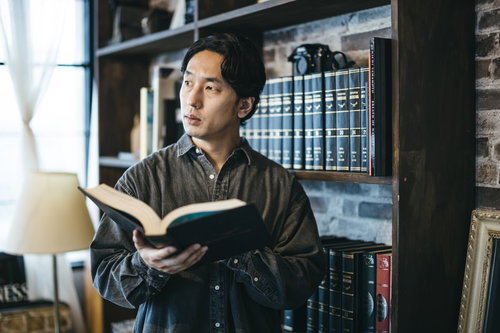 図書館で本を読みながら考えごとをする男性