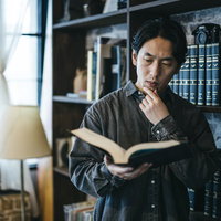 分厚い百科事典を広げて調べる男性の学習風景の写真