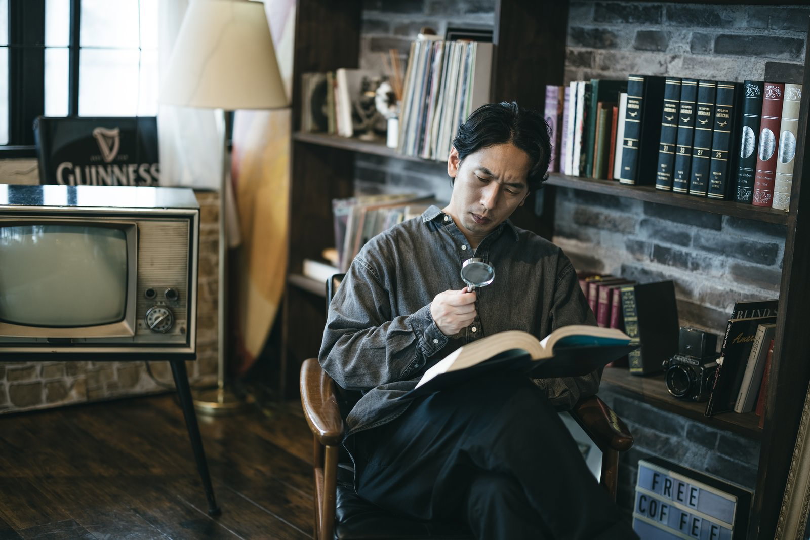 図書館の椅子に座って本を読んでいる男性［モデル：大川竜弥］
