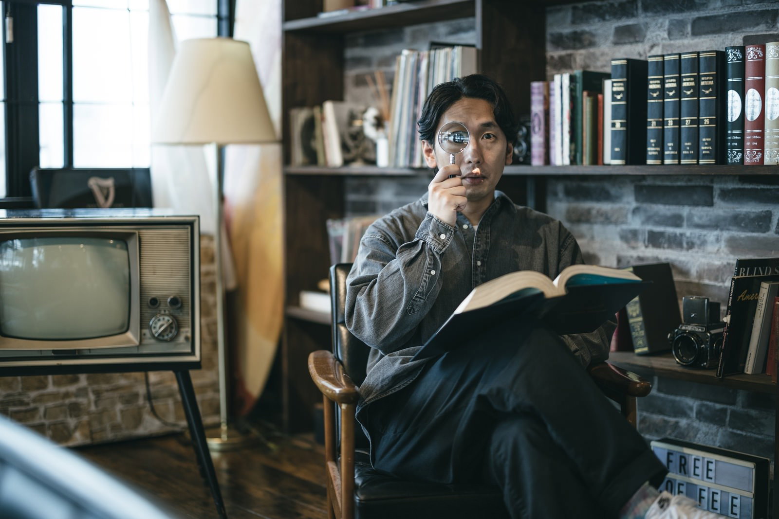 室内で拡大鏡を右目に当てながら本を読んでいる男性［モデル：大川竜弥］