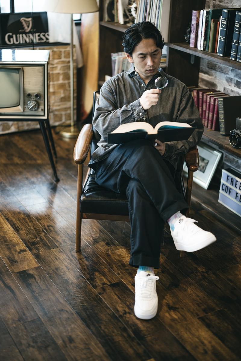 書斎で拡大鏡を使って本を読んでいる男性［モデル：大川竜弥］