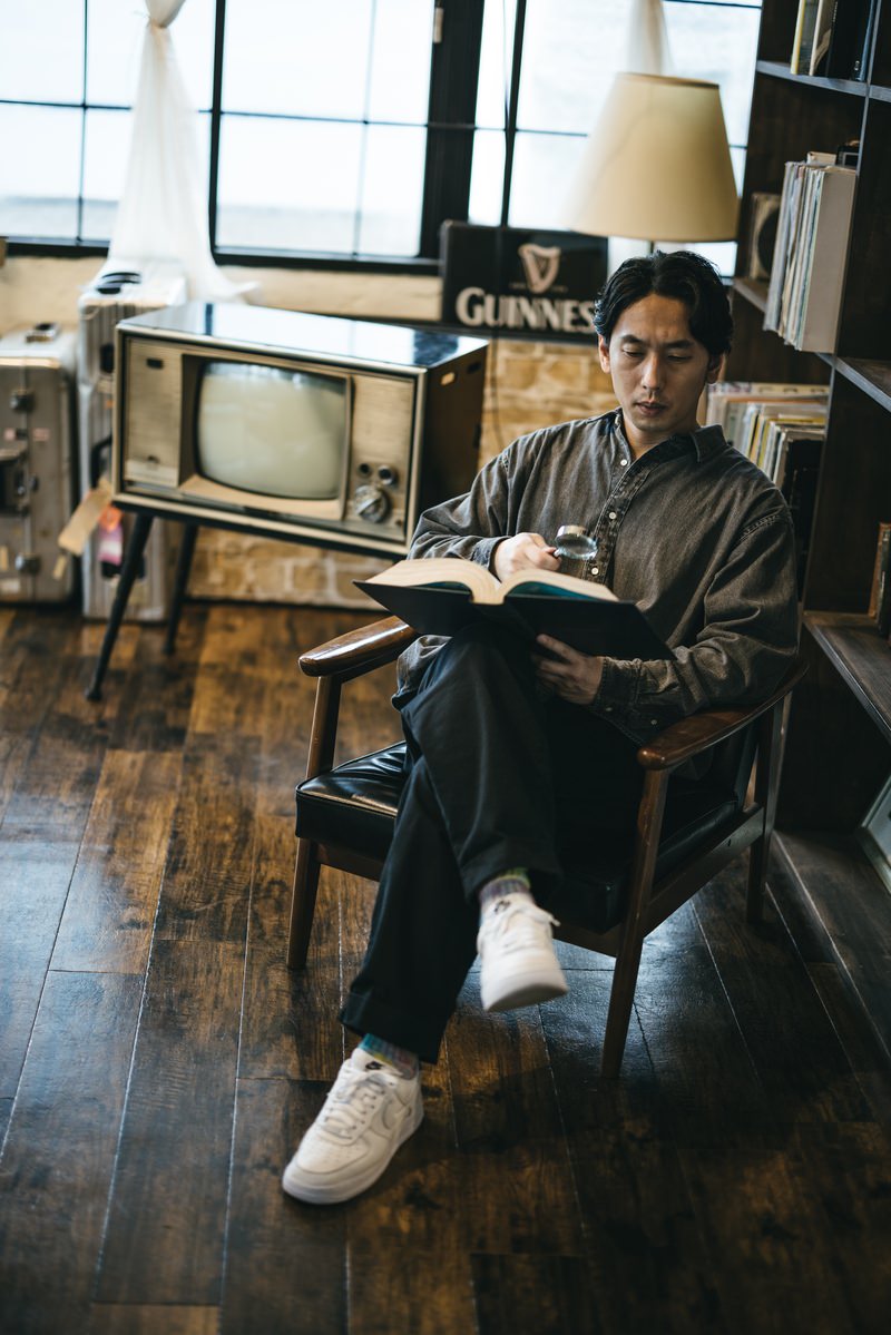 書斎で本を読みながら虫眼鏡を持つ男性［モデル：大川竜弥］