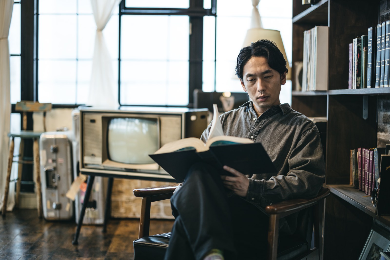 本棚に囲まれた書斎で洋書を読む男性［モデル：大川竜弥］