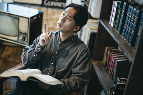 書斎で本を手に何かを思いつく男性、ひらめきの瞬間