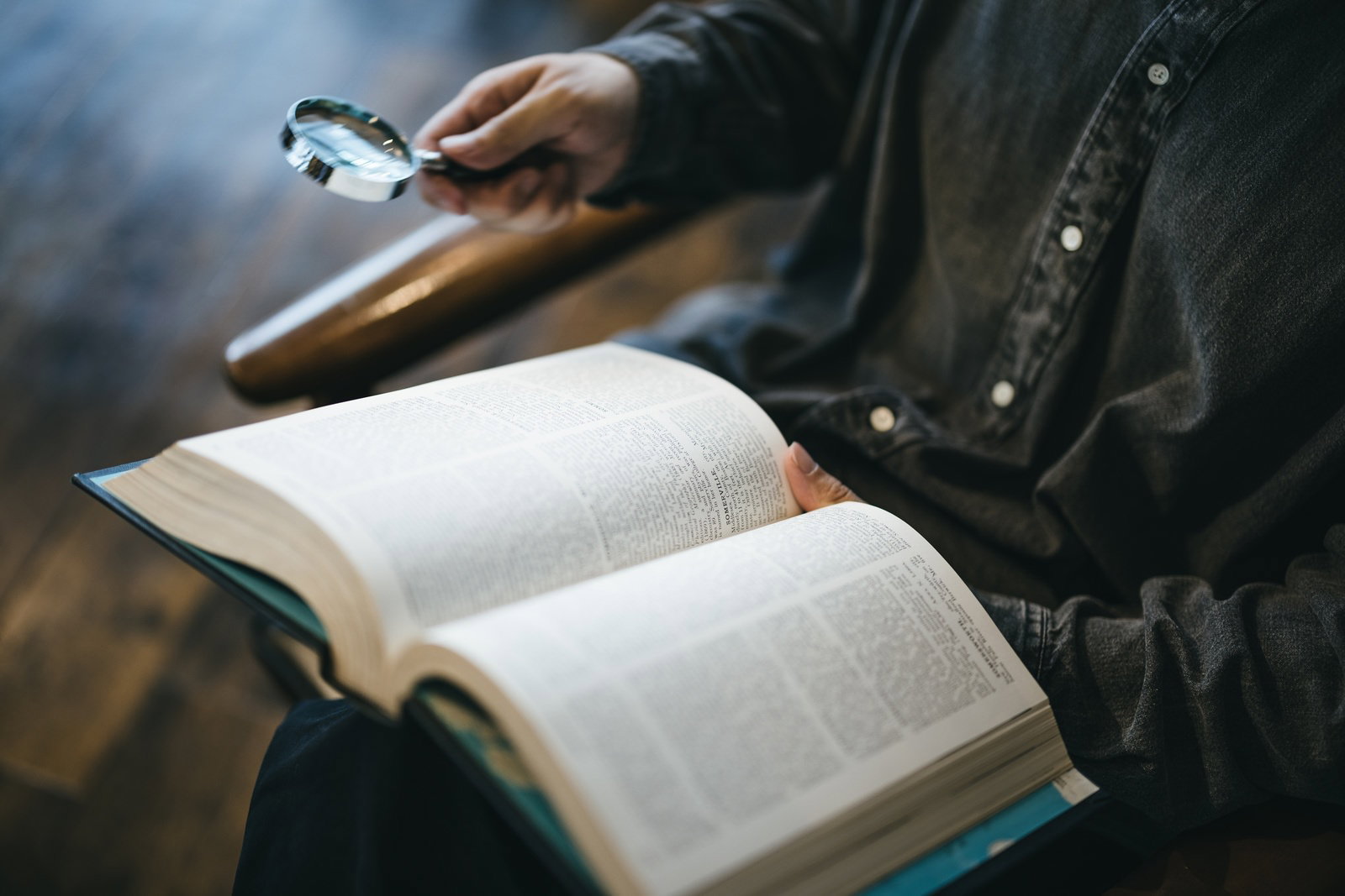 拡大鏡で本のページを調べながら読む人物［モデル：大川竜弥］