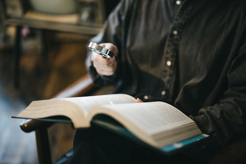 聖書をルーペで調べものをする手元の研究風景