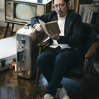 キャリーケースに寄りかかりながら洋書を読む男性の写真