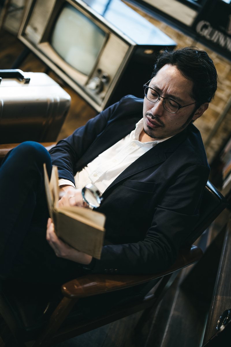 図書館でルーペを使って本を読む眼鏡をかけた男性［モデル：ゆうせい］