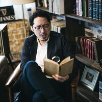本棚の前で眼鏡をかけて読書に集中する男性の写真