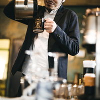 コーヒーカップにコーヒーを注ぐ眼鏡の男性の写真