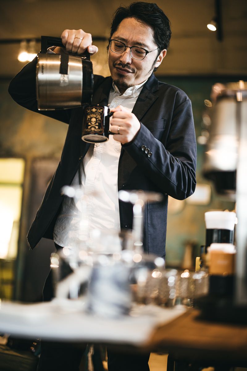 黒いジャケットを着た眼鏡の男性がコーヒーを注いでいる［モデル：ゆうせい］