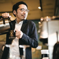 朝、出社後にコーヒーを飲みながら考える男性の写真