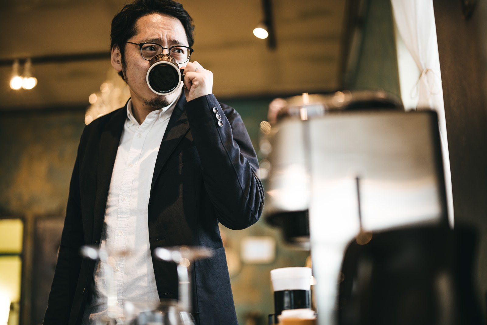 カフェでコーヒーを飲みながらくつろぐ眼鏡をかけた男性［モデル：ゆうせい］