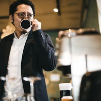 眼鏡をかけてコーヒーを飲む男性がカフェで休憩する様子の写真