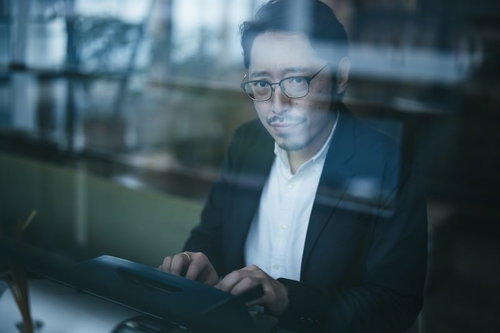 眼鏡をかけながらタイプライターで報告書を作る男性