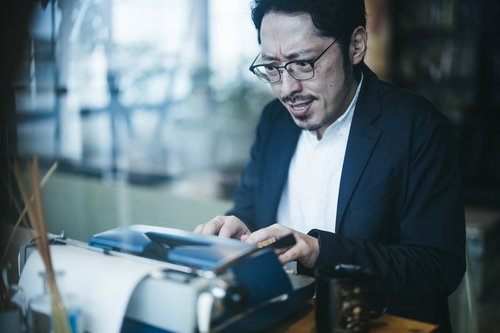 眼鏡をかけてしかめっ面でタイプライターをたたく男性