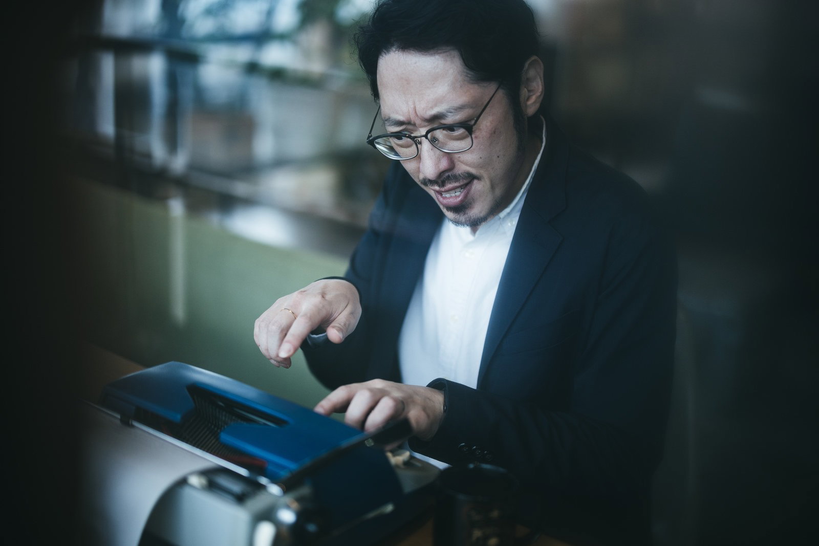 眼鏡をかけた男性がしかめっ面でタイプライターのキーを操作している手元［モデル：ゆうせい］