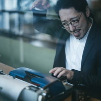 薄暗い部屋でタイプライターを操作する眼鏡の男性の写真