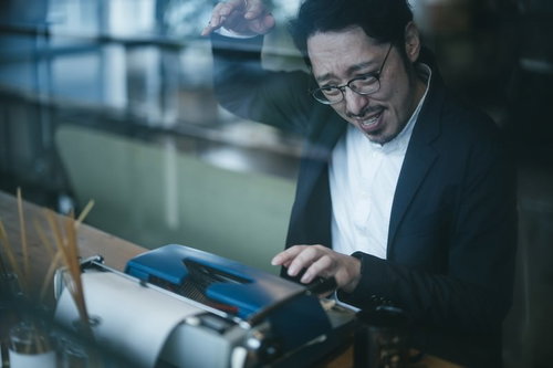 薄暗い部屋でタイプライターを操作する眼鏡の男性